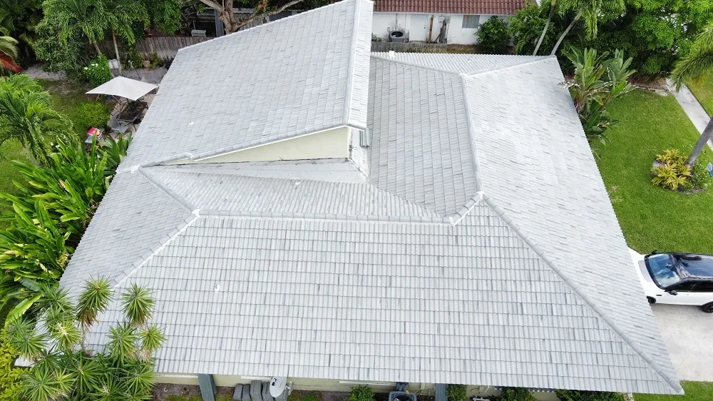 Aerial view of a light gray barrel tile roof with several hips and a valley on a single-story home with palms and a lawn