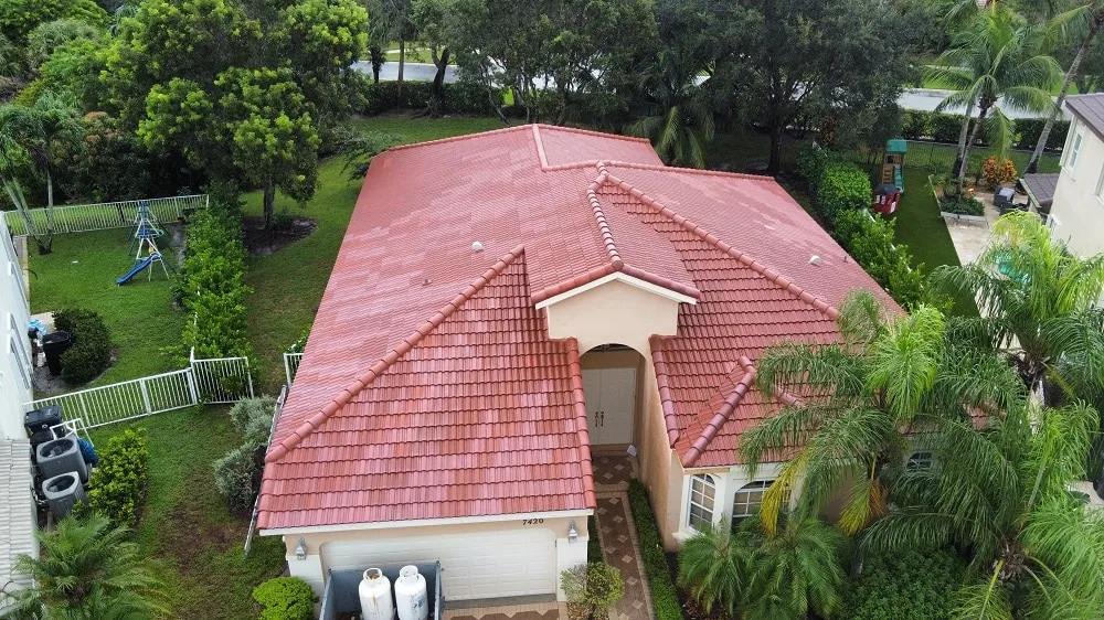 Aerial view of a single-story stucco home with a red barrel tile roof, a two-car garage, palm trees and a fenced yard