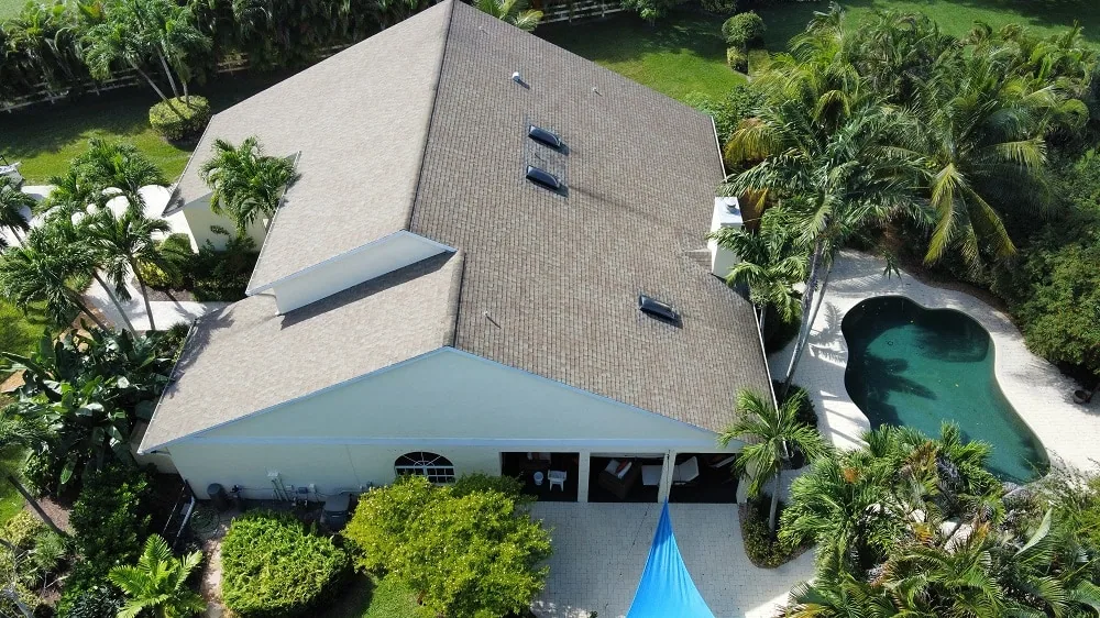 Aerial view of a home with a new tan shingle roof, three skylights, a covered patio, and a kidney-shaped pool surrounded by