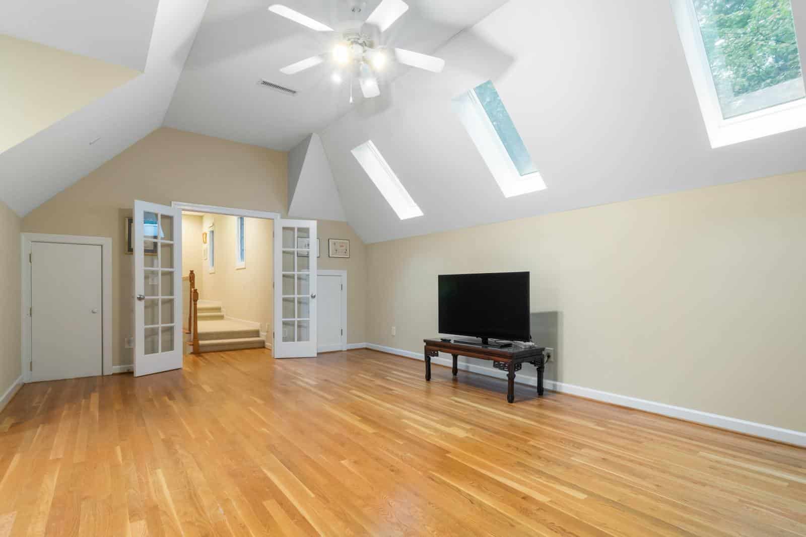 Bright attic room featuring skylights, wooden floors, and a TV setup, perfect for modern living.